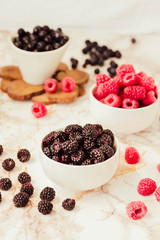 Raw raspberries and wild black, blackberries in white cups. Light marble background. Summer fruit, berries. Detox diets and healthy food concept.Selective focus.