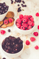 Raw raspberries and wild black, blackberries in white cups. Light marble background. Summer fruit, berries. Detox diets and healthy food concept.Tone.