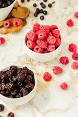 Raw raspberries and wild black, blackberries in white cups. Light marble background. Summer fruit, berries. Detox diets and healthy food concept.