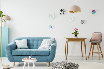 Comfy sofa, coffee table, pouf, wooden table and chair, and hanging patterned plates in a sweet living room interior - obrazy, fototapety, plakaty