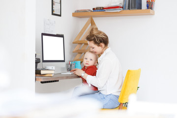 Attractive young pensive mother engineer works remotely at home and engaged in raising a child....