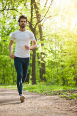 Young man is jogging in park. He is listening music on headphones.