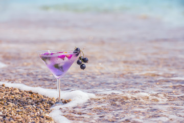 Fototapeta na wymiar refreshing summer drink in a glass on the beach, sparkling drops of water and pebbles in the surf line. Art photo with the mood of summer and rest. very selective soft focus 