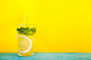 Glass with organic and fresh lemonade over yellow background on blue wooden board