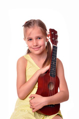 Cowgirl playing ukulele on a wooden chair, isolated on white background. Little girl with ukulele guitar.