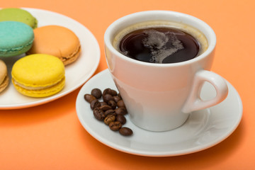 Cup of coffee with coffee beans and delicious macarons cakes of different color on white porcelain plate