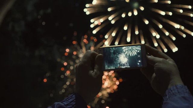 Silhouette of a man photographing fireworks at night sky. Beautiful salute in honor of the holiday.