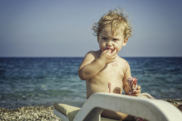 Baby boy eating icecream on the beach