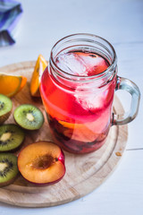 Glass mug with fruit drink with ice on a board with sliced fruit
