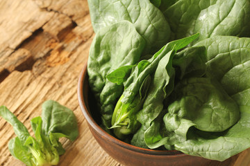 Fresh green leaves of spinach in a bowl on old wooden background.