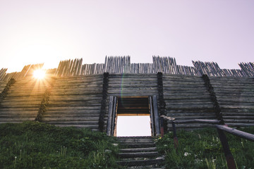 The old wooden gate and strengthened palisade,  through the barrier sun is shining