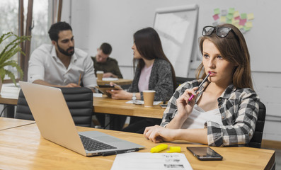 Fair-haired thinking girl in casual checked shirt having working at the laptop computer, indoor shot in cozy white office