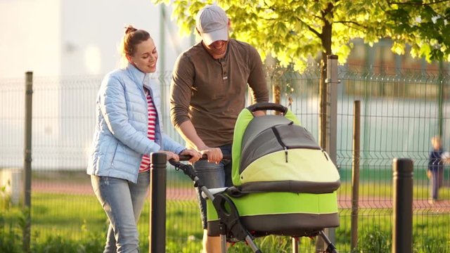 A young family, husband and wife on a walk with their newborn baby in a baby carriage. A happy family. Family day