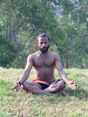 Naklejka na ściany i meble Athletic Indian man meditating in lotus yoga pose in forest