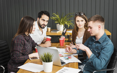 Team of young apprentices talking about the project, working discussion at brown office desk, concept of teamwork