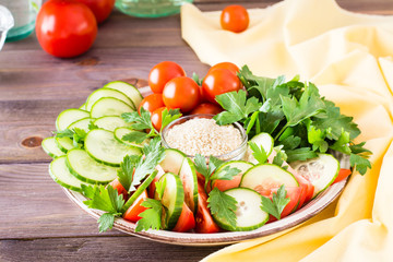 Fresh slices of cucumbers, tomatoes and parsley leaves on a plate on a wooden table