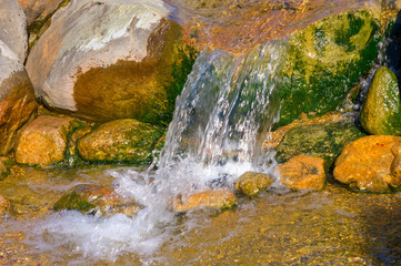 Small waterfall on forest river. Small stream with stones and waterfall in sunny weather