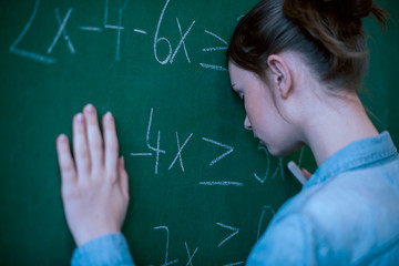 Teenager girl in math class overwhelmed by the math formula. Pressure, Education, Success concept. Student with head against blackboard.