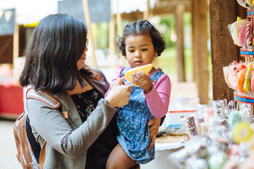 Mexican mother with dark skinned hispanic toddler girl delighted with choosing lollipop in candy...