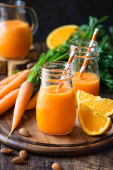 Healthy detox orange carrot smoothie or juice in glass jars on wooden background with fresh...