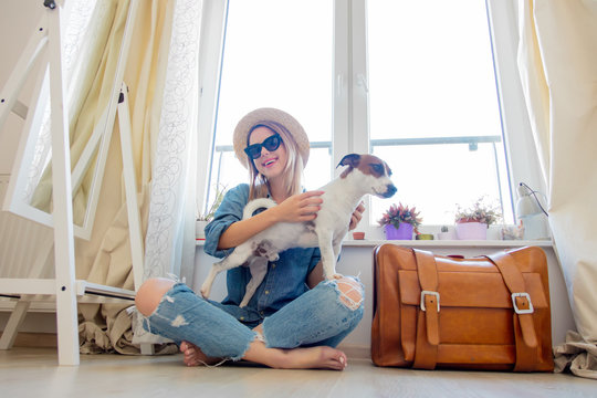 Young girl with dog sitting next to suitcase before travel near a window at home