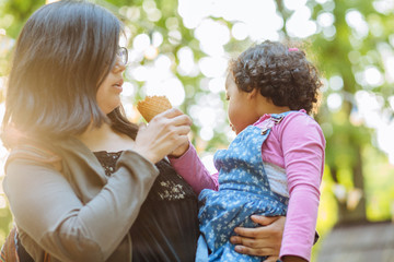 Obraz premium latino american mother and dark skinned hispanic toddler daughter eating ice-cream during a walk outdoors.