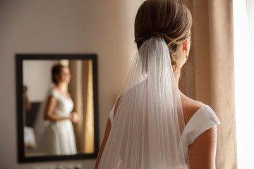 Beautiful bride in white wedding dress. Fitting room with reflection of bride in mirror and copy...
