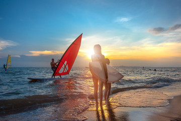 slim woman with family group father, sister are enjoy around with water sports such surfboard, windsurf, kitesurf in the sea beach at sunset scenery
