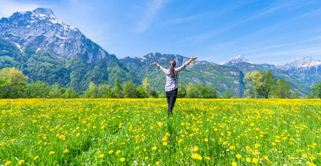 Joyful Summer. Woman with open hands on the field of flowering dandelions. Summer landscape against the background of mountains.