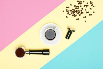 Cup of black coffee, portafilter and tamper on pastel coloured background. Coffee preparation concept.