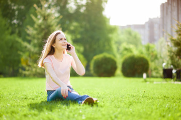 Naklejka na ściany i meble Girl talking on the phone sitting in the Park on the grass