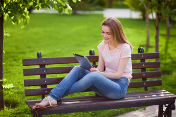 Obraz premium Girl with tablet sitting on a bench in the Park