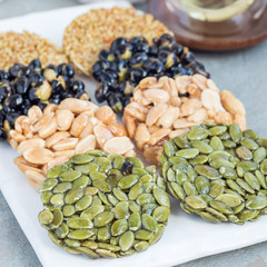 Korean traditional sweet snacks with peanuts, pumpkin seeds, black soybeans and chinese buckwheat on white plate, square format