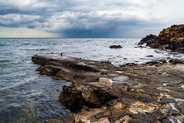 Fototapeta na wymiar Western Kullaberg nature reserve, Sweden - Storm clouds approaching over the small stone pier in the rocky landscape.
