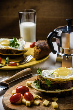 Dish of sandwich with fried eggs, cucumbers and cherry-tomatoes with bread and milk on linen tablecloth, dark and moody.