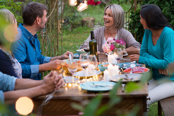 Beautiful summer evening in the garden, a group of friends in their forties have a good time laughing together around a table.