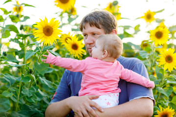 Happy proud young father with cute baby daughter in sunflower field, family portrait together