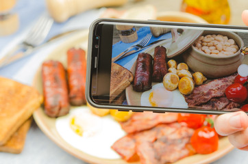 Man taking photo of traditional full English breakfast on smartphone. Taking food photo with mobile...