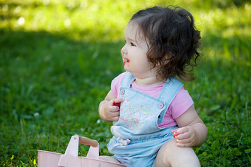 Happy smiling baby girl eating summer raspberries. Sitting in the grass, enjoying the nature
