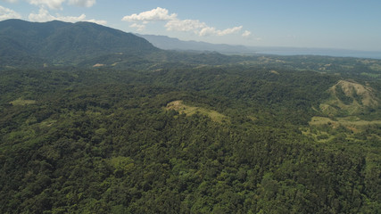 Aerial view of mountains covered with green forest, trees with blue sky. Philippines, Pagudpud, Luzon. Tropical landscape in Asia.