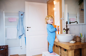 Cute toddler boy standing on a stool in the bathroom.