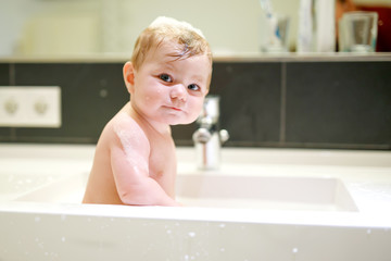 Cute adorable baby taking bath in washing sink and playing with water and foam
