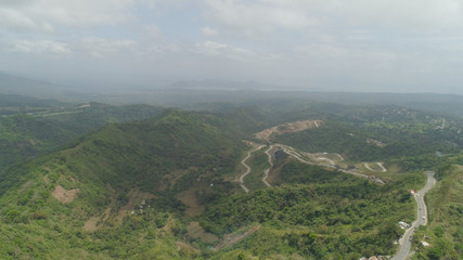 Aerial view of road, mountains covered forest, trees. Cordillera region. Luzon, Philippines. Slopes of mountains with evergreen vegetation. Mountainous tropical landscape.