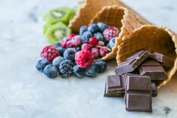 Healthy diet concept - fruits and frozen berries in ice cream cones on rustic background