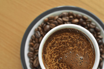 A cup of coffee with foam on a saucer with coffee beans