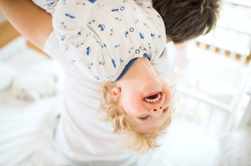 Father holding a happy toddler boy upside down.