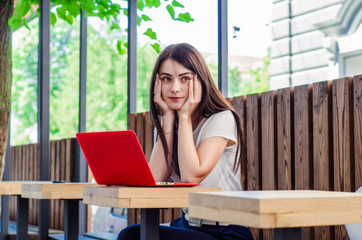 Beautiful girl sitting at a table in a street cafe with a red laptop