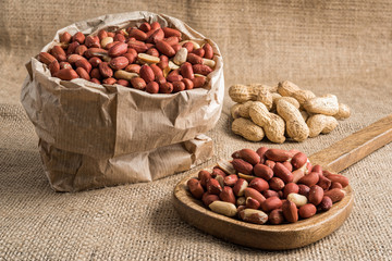 Peeled peanuts in a wooden ladle and paper bag full of peeled peanuts and peanuts in nutshell on sackcloth