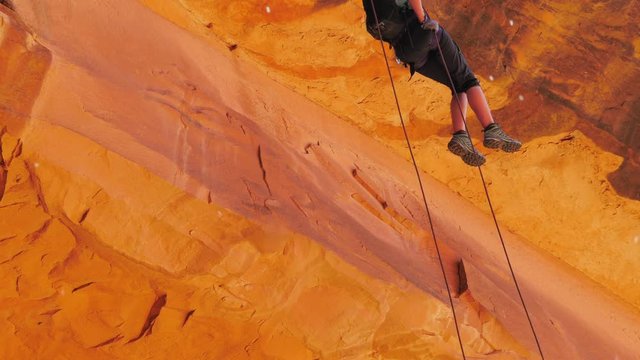Girl slowly descending on a rope rappelling down sandstone.