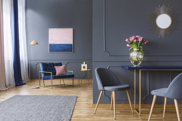 Pink flowers on table in grey elegant living room interior with gold mirror and painting